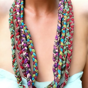 Puede incluir: Un collar trenzado multicolor hecho de retazos de tela. El collar es largo y de capas, con una variedad de colores y patrones.