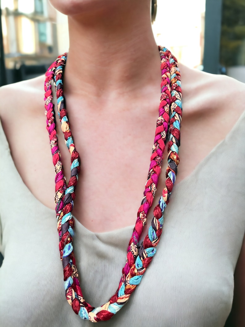 Op de afbeelding: Een lange, veelkleurige gevlochten ketting gemaakt van stof. De ketting is gemaakt van rode, blauwe, bruine en witte stof.