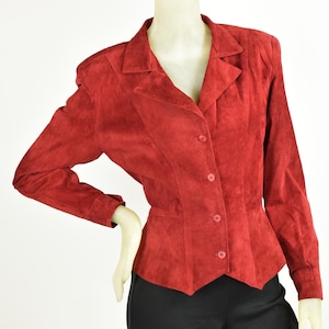 Op de afbeelding: Een rood suède jack met een knoopsluiting en een getailleerde pasvorm. Het jack heeft lange mouwen en een puntige kraag.