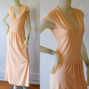 May include: A long peach-colored maxi dress with a V-neckline and short sleeves. The dress has a gathered waist and a flowing skirt.