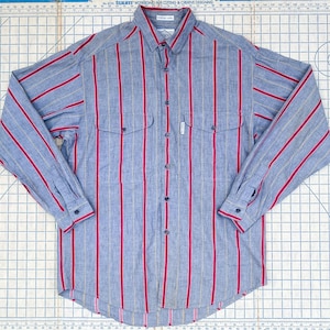 Puede incluir: Una camisa de manga larga con botones a rayas azules y rojas con una etiqueta blanca que dice "Pacific Trail" en la parte delantera.