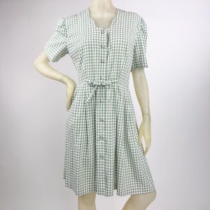 May include: A light green and white gingham dress with short sleeves and a V-neckline. The dress features a button-down front, a tie-waist, and a knee-length skirt. The dress is displayed on a mannequin.