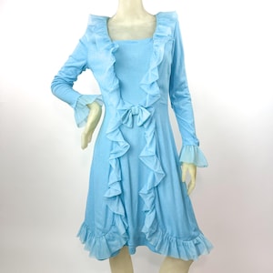 May include: A light blue dress with long sleeves and a square neckline. The dress features ruffled trim along the front, neckline, and hem, with a bow detail at the waist. The sleeves have sheer, flared cuffs.