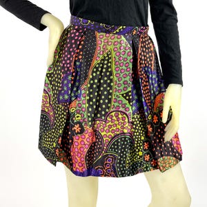 May include: A colorful, patterned skirt with a black background. The skirt features a vibrant mix of pink, orange, green, and purple floral and polka dot designs. The skirt is pleated and appears to be made of a silky material.