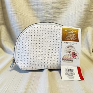 May include: A white semi-circular pouch with a perforated texture and a silver zipper closure. A product tag is attached, featuring the text embroidery pouch and illustrations of three pouches with different decorative patterns.