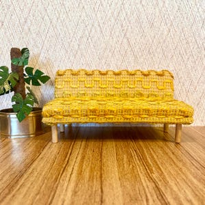 May include: A small yellow couch with a woven fabric upholstery and wooden legs. The couch is sitting on a wooden floor.