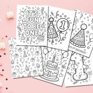 May include: A set of black and white birthday-themed colouring pages. The designs include birthday cakes, balloons, party hats, and the phrases "IT'S FUN TO BE ONE" and "HAPPY 1ST BIRTHDAY!". The pages are arranged on a pink surface.
