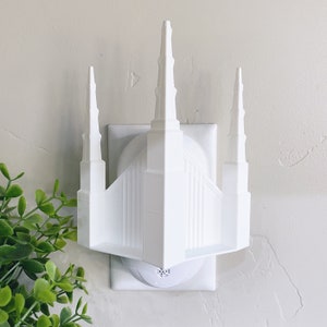 May include: White plastic night light shaped like a temple with three spires. The night light plugs into a standard electrical outlet.