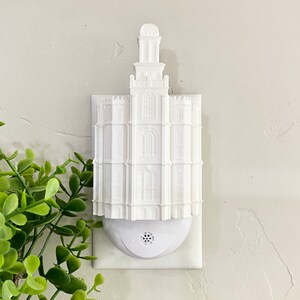 May include: White night light shaped like a temple with a white electrical outlet.