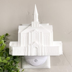 May include: White plastic nightlight shaped like a church building. The nightlight plugs into a standard electrical outlet.