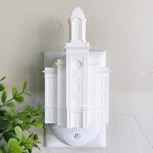 May include: White plastic night light shaped like a temple. The night light plugs into a standard electrical outlet.