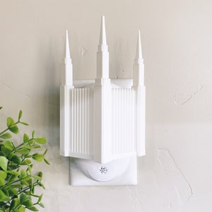 May include: White plastic nightlight shaped like a temple with three spires. The nightlight plugs into a standard electrical outlet.