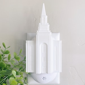 May include: White plastic night light shaped like a temple. The night light plugs into a standard electrical outlet.