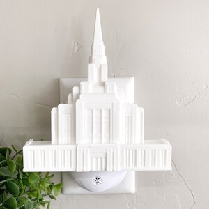 May include: White plastic night light shaped like a temple. The night light plugs into a standard electrical outlet.