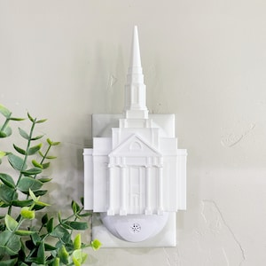 May include: White plastic night light shaped like a temple. The night light plugs into a standard electrical outlet.