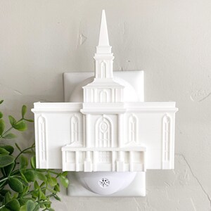 May include: White plastic night light shaped like a temple. The night light plugs into a standard electrical outlet.