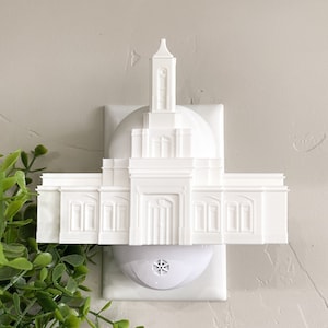 May include: White plastic nightlight shaped like a temple. The nightlight is plugged into a standard electrical outlet.