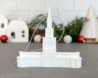 Op de afbeelding: Witte 3D-geprinte ornament van een kerkgebouw met een toren. De ornament heeft een zilveren touwtje om op te hangen.