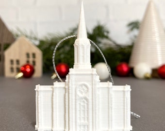 May include: White 3D printed ornament of a church building with a spire. The ornament is hanging from a silver string.