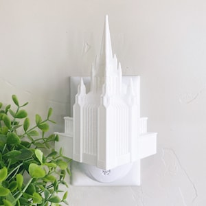 May include: White plastic nightlight shaped like a church building. The nightlight is plugged into a standard electrical outlet.