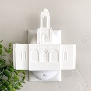 May include: White plastic night light shaped like a temple with a dome and a spire. The night light plugs into a standard electrical outlet.