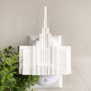 Op de afbeelding: Witte plastic nachtwacht in de vorm van een tempel. De nachtwacht steekt in een standaard stopcontact.