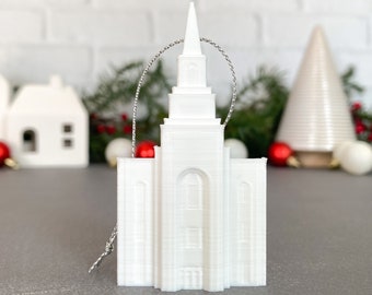 Op de afbeelding: Witte keramische ornament in de vorm van een tempel met een zilveren touwtje om op te hangen.