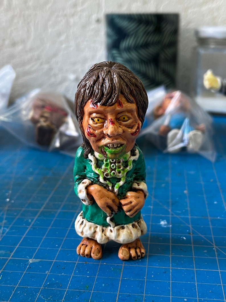 May include: A small green and white figurine of a person with a green face and yellow eyes. The figurine is wearing a green robe with white trim and has a green snake around its neck.