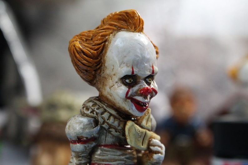 Puede incluir: Primer plano de una figura de payaso con maquillaje rojo y blanco, pelo naranja y una sonrisa de dientes. La figura lleva un cuello de volantes blanco y rojo.