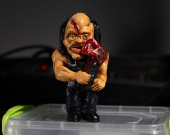 Könnte beinhalten: Eine kleine, handbemalte Figur eines Horror-Charakters mit einer blutigen Axt. Die Figur ist aus Ton gefertigt und hat ein realistisches Aussehen. Der Charakter hat ein entstelltes Gesicht mit einer großen Narbe und eine blutige Axt in der Hand.