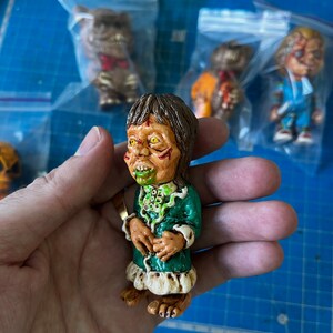 May include: A small green and white figurine of a monster with a green face and yellow eyes. The monster is wearing a green dress with white trim and has a green and white necklace.