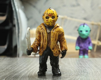 May include: A small plastic figurine of a horror movie character wearing a yellow jacket and a white hockey mask. The character is holding a silver knife in their right hand.
