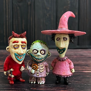 Pode incluir: Três figuras feitas à mão do filme O Estranho Mundo de Jack. As figuras são de Lock, Shock e Barrel. Lock está vestindo um terno vermelho e segurando um bastão de doces. Shock está vestindo um vestido roxo e branco e segurando uma pirulito. Barrel está vestindo um vestido rosa e um chapéu de bruxa rosa.