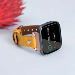 May include: A yellow leather band with a black and silver fitness tracker. The tracker displays 12,000 steps and 67 bpm.