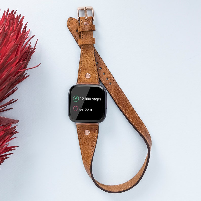 May include: A brown leather band with a rose gold buckle for a fitness tracker. The tracker screen displays "12,000 steps" and "67 bpm".