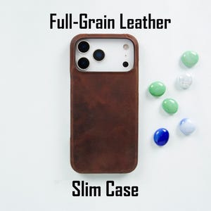 May include: A dark brown full-grain leather slim case for a smartphone with a triple-lens camera cutout. The text Full-Grain Leather is printed above the case and Slim Case is printed below it, accompanied by several small, smooth glass pebbles.