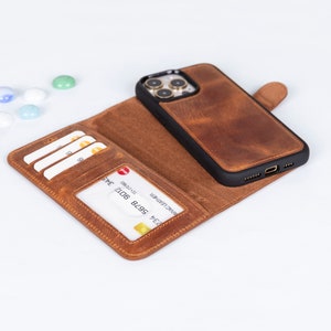 May include: A brown leather phone case with a wallet design. The case has a black frame and a magnetic closure. The wallet section features card slots and a clear ID window. The case is open, displaying the interior and a credit card.