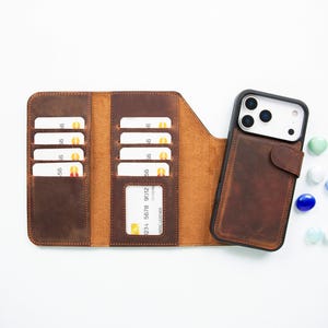 May include: A brown leather wallet phone case with a tri-fold design, featuring multiple interior card slots and a clear ID window. The case includes a dedicated compartment for a smartphone with a triple-lens camera cutout and a magnetic strap.