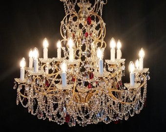 May include: A large, ornate gold chandelier with crystal drops and red accents. The chandelier has multiple arms and is lit by many small light bulbs.