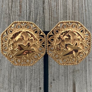 May include: A pair of gold-tone clip-on earrings featuring a delicate filigree design and a raised floral motif.
