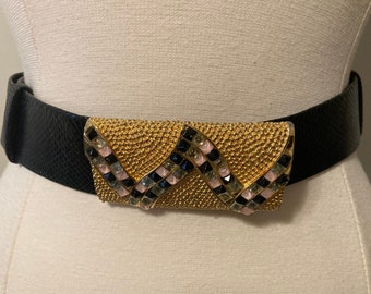 Könnte beinhalten: Ein schwarzer Ledergürtel mit einer goldfarbenen Schnalle, die mit rosa, schwarzen und klaren Strasssteinen verziert ist. Die Schnalle hat ein geometrisches Design.