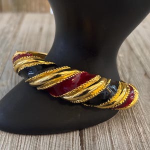 Op de afbeelding: Een gouden, zwart en rood geëmailleerde armband met een gedraaid ontwerp.