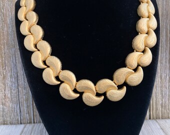 May include: A gold-tone necklace with a chain made of interlocking leaf-shaped links.