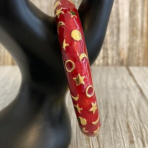 May include: Red enamel bangle bracelet with a gold design of stars, moons, and circles.