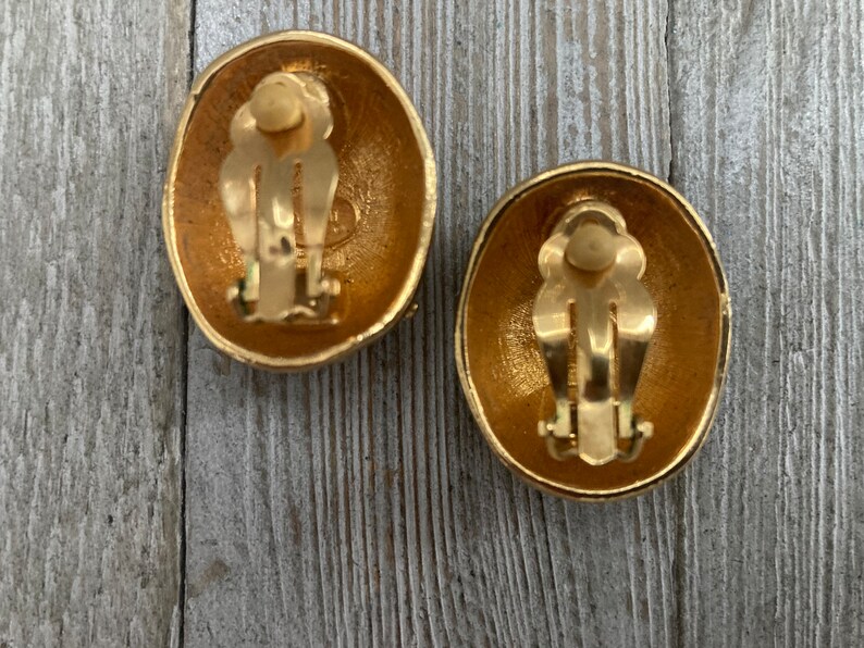 May include: A pair of gold-tone oval-shaped clip-on earrings. The earrings have a textured surface and a simple design.