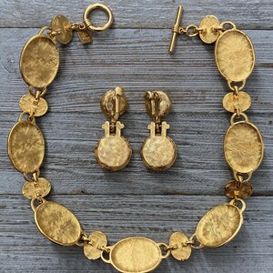 Pode incluir: Um conjunto de colar e brincos em tom dourado com elos de forma oval. O colar tem um fecho de trava e os brincos t&ecirc;m um fecho de press&atilde;o.