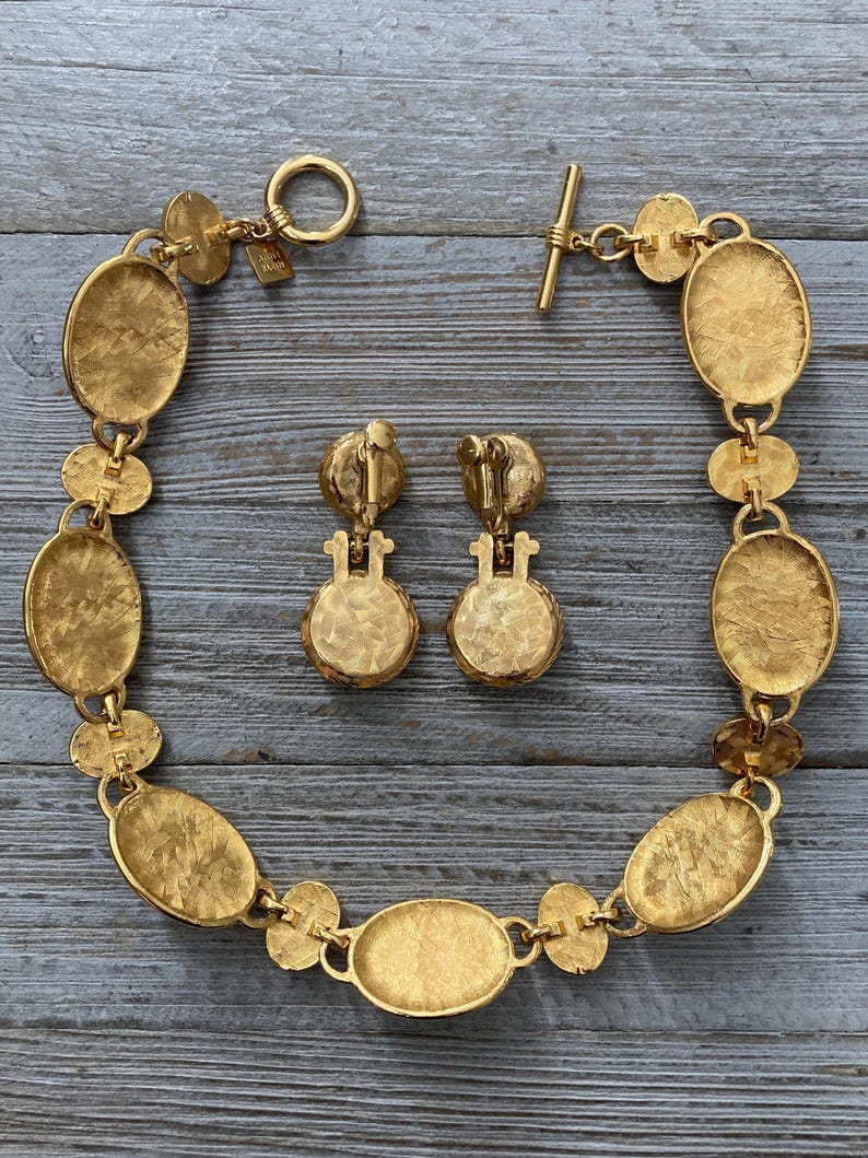 Pode incluir: Um conjunto de colar e brincos em tom dourado com elos de forma oval. O colar tem um fecho de trava e os brincos t&ecirc;m um fecho de press&atilde;o.