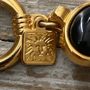 Pode incluir: Chaveiro dourado com uma pedra de &ocirc;nix preta e um logotipo de cabe&ccedil;a de le&atilde;o. O chaveiro tem um anel para prender as chaves.