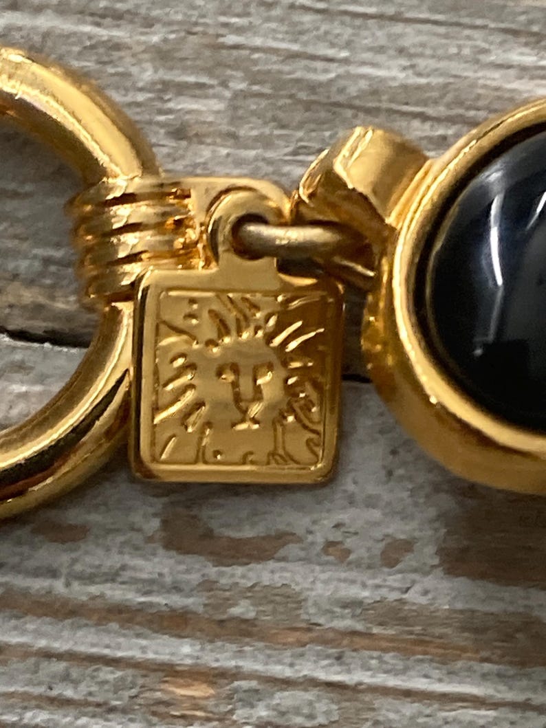 Pode incluir: Chaveiro dourado com uma pedra de &ocirc;nix preta e um logotipo de cabe&ccedil;a de le&atilde;o. O chaveiro tem um anel para prender as chaves.