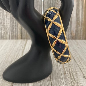 May include: A gold and navy blue bangle bracelet with a geometric pattern. The bracelet is made of metal and has a shiny finish.